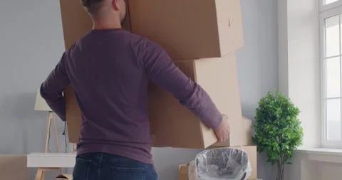 Clumsy guy holding boxes in hands losing his balance and falling on the floor in Stock Footage 270207691