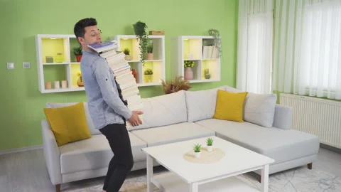 Clumsy young man drops a pile of books at home. Stock Footage 232289404