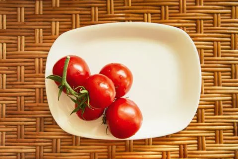 A cluster of red cherry tomatoes on a white flat rectangular plate stand on a Stock Photos