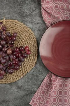 Cluster of red grapes and empty red plate on marble surface Stock Photos