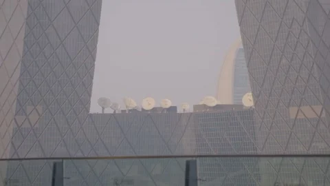 Cluster of Satellite Dishes on Rooftop Framed by CCTV Headquarters Beijing China Stock Footage 341712898