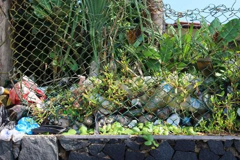 Clutter of plastic bottles, waste, vegetation piled against a chain-link fence Stock Photos