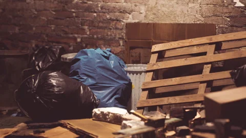 Cluttered basement storage area with debris and trash bags in a dimly lit space Stock Footage 304467777