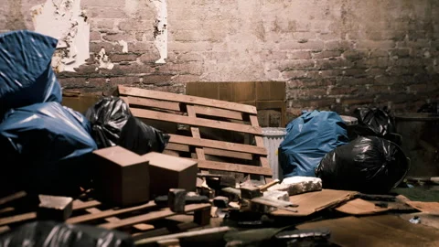 Cluttered basement with trash bags pallets and scattered debris in dim light Stock Footage 304467787