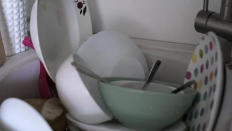 A cluttered kitchen sink filled with dishes, cups, and utensils, illustrating Stock Footage 293772150