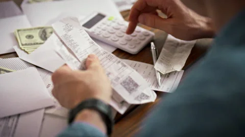 At a cluttered kitchen table a man taps a calculator amid checks and cash-fi Stock Footage 338186503