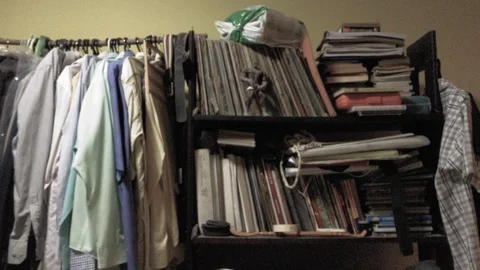 Cluttered messy wardrobe with stacked clothes and dusty books in front of a Stock Footage 92558136