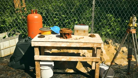 A cluttered outdoor work area with a table, ladder, and various tools in front Видео 309072295