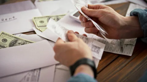 At a cluttered table a man uses a calculator while sorting receipts and bank Stock Footage 336570674