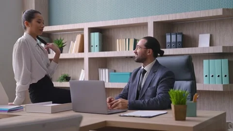 A co-worker is sitting on the table in front of the man, flirting, talking Stock Footage 233994469
