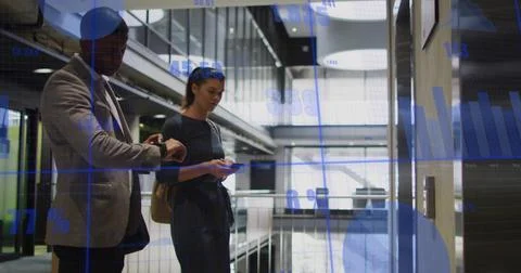 Co-workers checking watch and browsing phone near elevator panel in office with Stock Photos