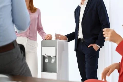 Co-workers having break near water cooler at workplace, closeup Stock Photos
