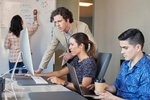 Co-Workers talking at computer in office while woman is working on dry erase Stock Photos