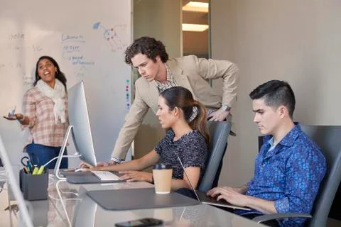 Co-Workers talking at computer in office while woman is working on dry erase Foto stock