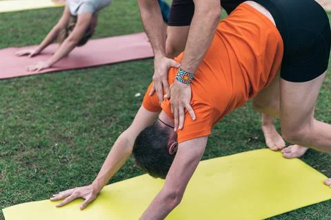 Coach correcting the yoga pose to a learner in an outdoor class Stock Photos