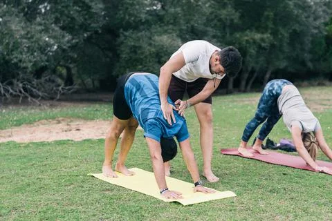 Coach correcting the yoga posture of a learner outdoors Stock Photos