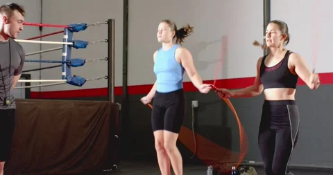 At coach count female trainees skipping orange jump ropes on red mat in gym Видео 345061993