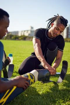 Coach helping young male amputee athlete with prosthetic in park Stock Photos