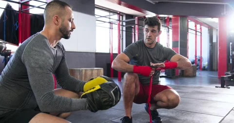 Coach raising mitts and trainee boxer wrapping red wrap for pad work at gym Stock Footage 341240327