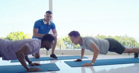 Coach timing reps, supervising two men tapping hands and doing pushups on blue Stock Footage 335780740