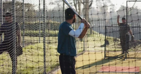 Coach tossing baseball toward mid adult player swinging silver bat on batting 動画素材 337096556