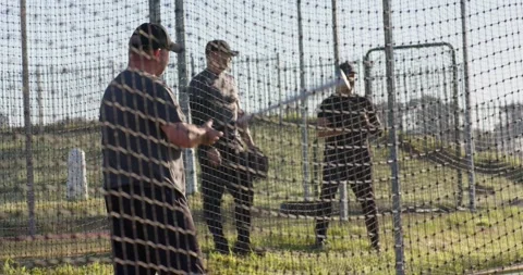 Coach tossing baseballs as batter swinging inside batting cage netting for Stock Footage 340610475