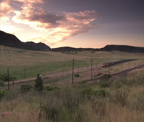 Coal train moving parallel to car on road at sunset Stock Footage 86692720