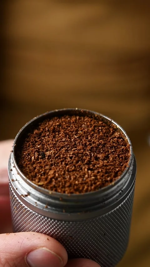 Coarse coffee grounds for cold brew are shown inside a metal grinder cup held by Stock Footage 346743712