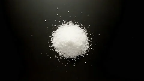 Coarse salt graines is piled up on the black table, stop motion, top view Vidéo 145631795