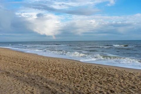 Coast with a wave rolling over it and a rainbow in the sky Stock Photos
