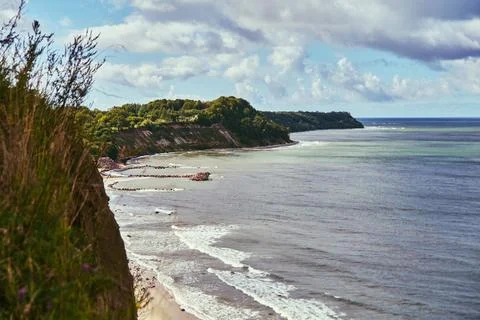 Coastal cliffs overlook quiet beach beneath dramatic cloudy light 스톡 사진