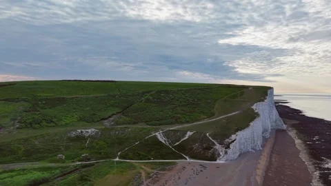 Coastal cliffside flight over white chalk cliffs and scenic beach at sunset Stock Footage 309765301