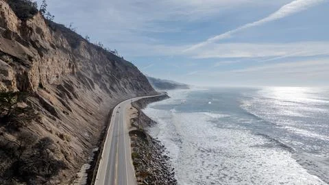 Coastal Highway Beneath Steep Cliffs on Sunny Pacific Shore Stock Photos