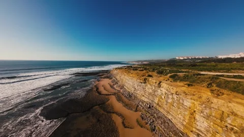 Coastal landscape with dramatic cliffs, waves, and sandy beach under bright sun Stock Footage 339787221