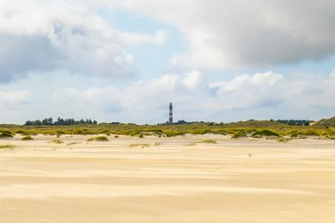 Coastal landscape featuring a distant lighthouse, rolling sand dunes, and a.. Stock Photos