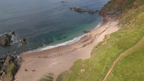 Coastal Path overlooking Sandy Beach &amp; Clear Blue Ocean - Aerial Drone Footage Stock Footage 160076114