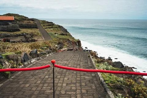 Coastal Path with Red Barrier Overlooking Ocean and Waves Under Cloudy Sky,.. Stock Photos