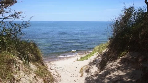 Coastal sandy path leading to calm blue sea bordered by green vegetation un.. Video stock 344302496