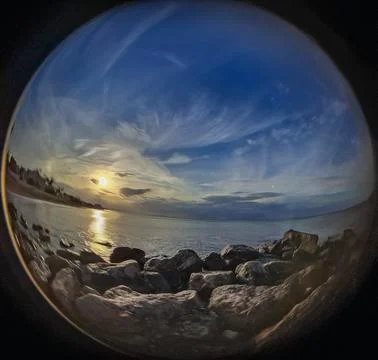 Coastal sunset viewed through a circular fisheye lens over a rocky beach at.. Photos