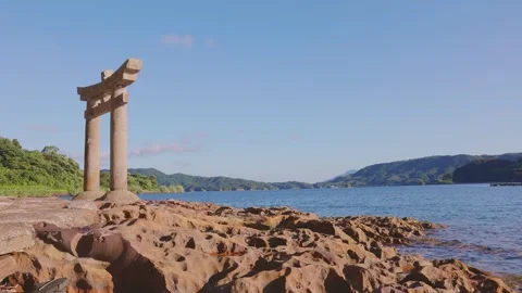 Coastal Torii gate on rugged eroded rock shore looking over calm ocean bay Video stock 340749748