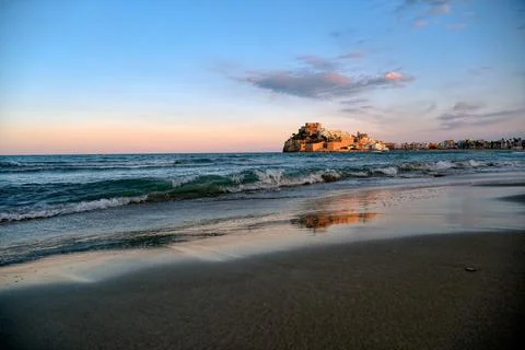 Coastal view at sunset with waves reflecting light and castle on the horizon Stock Photos