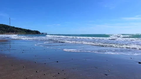 Coastal waves rolling onto sandy beach under blue summer sky Stock Footage 310243095
