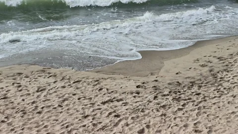 Coastal waves rolling toward sandy shoreline beneath gray overcast sky Video stock 343627945