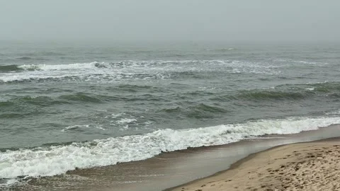 Coastal waves rolling toward sandy shoreline beneath gray overcast sky Stock Footage 343628241