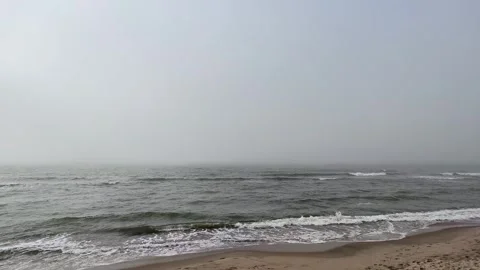 Coastal waves rolling toward sandy shoreline beneath gray overcast sky Stock Footage 343628253
