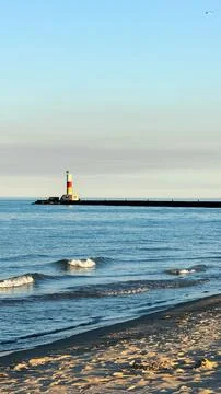 Coastline view at sunset with waves a lighthouse and a pier along the shore Photos
