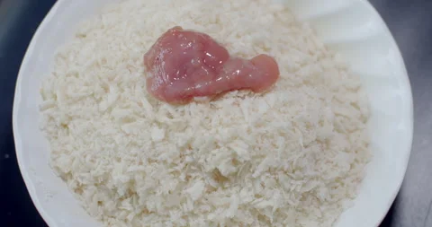 Coating egg-dipped pork slices with breadcrumbs to create a crispy outer layer. Stock Footage 312311947