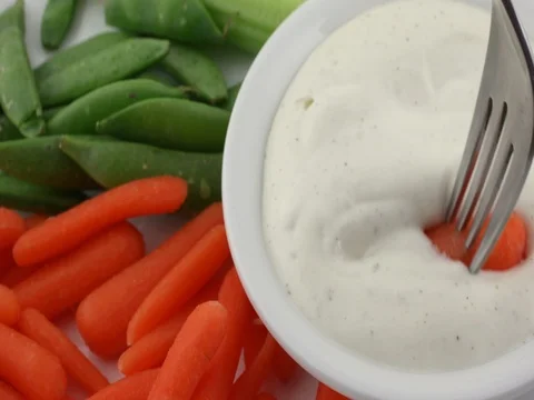 Coating a peeled carrot on a fork with ranch dressing Stock Footage