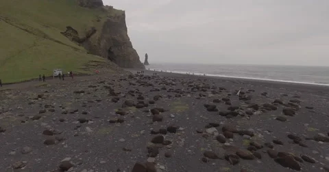Cobbled black beach below a green cliff and sea stack Vidéo 64072178