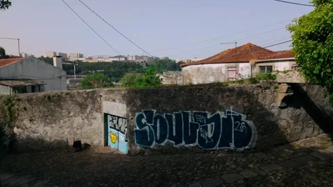 Cobbled path descending past old stone wall with vibrant graffiti art in Porto 库存影片 334614665